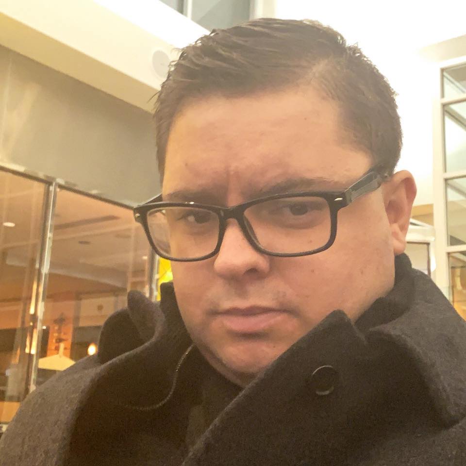 Photo of Mike Pinola wearing black plastic full-rim eyeglasses. Slicked and short hair parted on his left side. He is wearing a heavy coat. He probably thinks he looks cool in this photo. He does not.