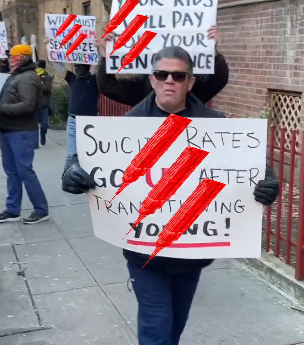 Tony Pagano in sunglasses at a DQSH protest in Jackson Heights. He's carrying a sign containing transphobic medical disinformation. Behind him are other Proud Boys on the sidewalk with similar signs. The other Proud Boys have masks on.